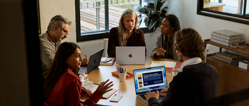 Cinq personnes réunies autour d’une table dans une salle de réunion, avec trois MacBook Pro.