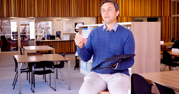 Photo d'un homme assis sur un tabouret avec un iPad dans les mains et un stylet