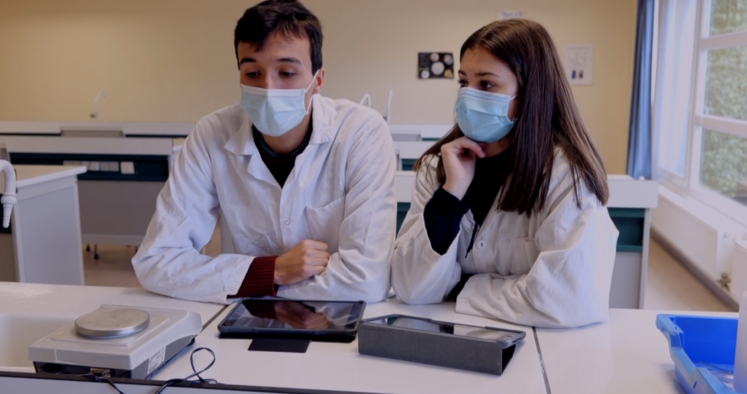 deux élèves portant des blouses et des masques dans un laboratoire et travaillant sur iPad