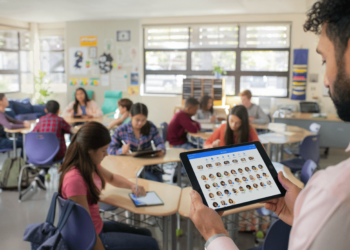 photo d'un professeur tenant un ipad dans les mains avec ses élèves assis en classe au second plan