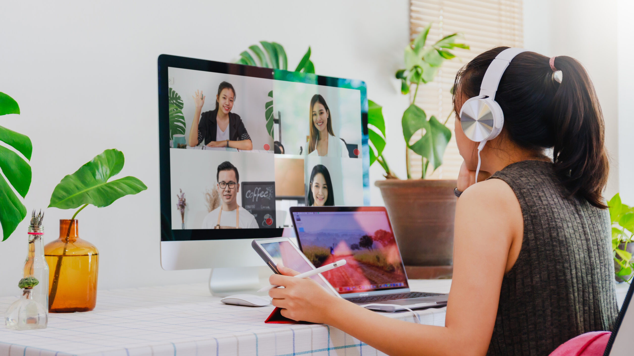 femme portant un casque en appel visio sur son iMac, avec son MacBook et son iPad sous les yeux