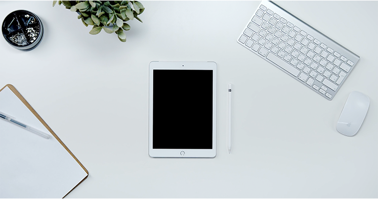 vue surplombante dun bureau sur lequel est posé un clavier, une souris, un iPad et un bloc note
