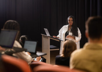 Femme présidant un conférence et s'appuyant sur ses notes sur son MacBook