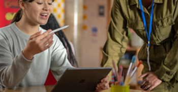 Une professeure aidant une étudiante assise en classe avec son iPad